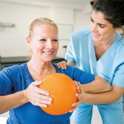 Dame macht Übung mit Ball, Ergotherapeutin unterstützt